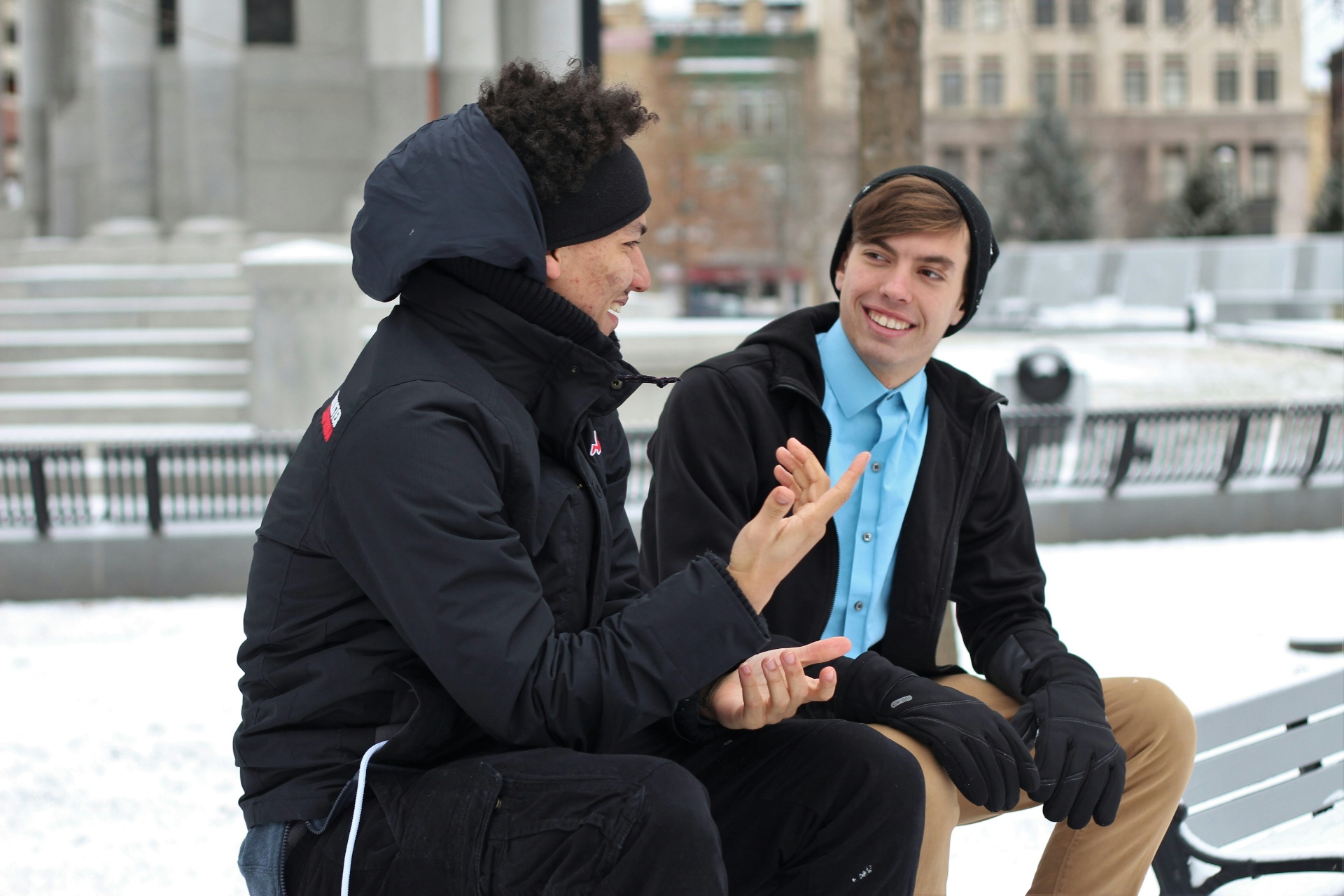 Deux hommes en conversation animée sur un banc en hiver, gestes ouverts et sourires — la relation humaine au cœur du changement.