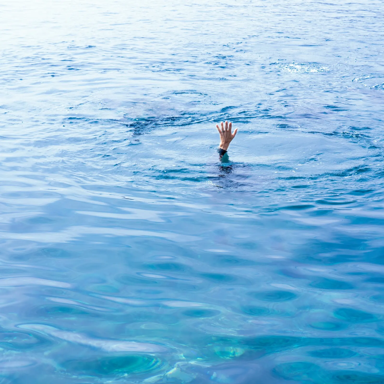 Une main émerge à la surface d'une eau turquoise — l'image silencieuse d'un appel à l'aide.
