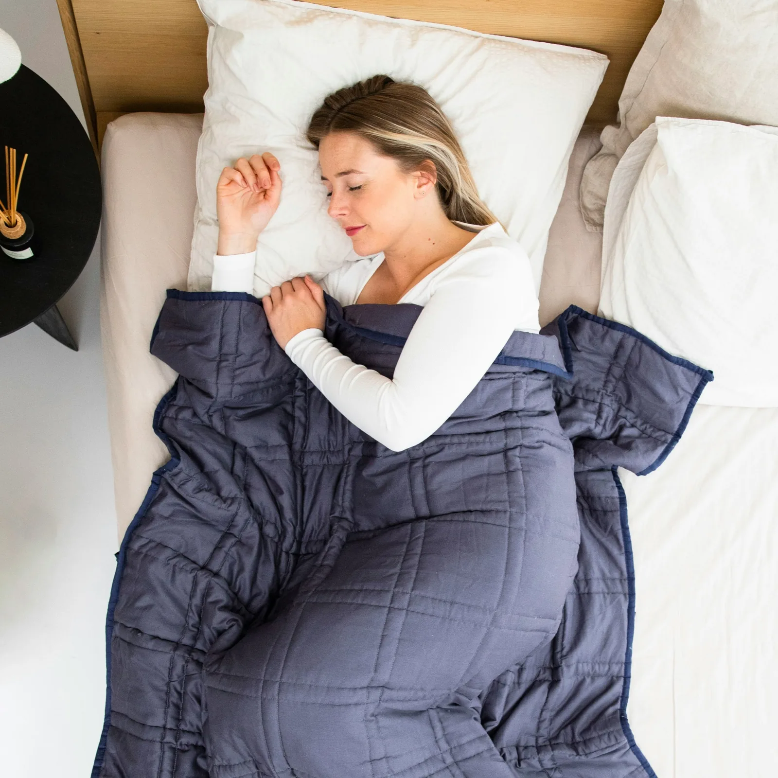 Une femme dort paisiblement sous une couverture lestée bleue — le sommeil comme fondation invisible.
