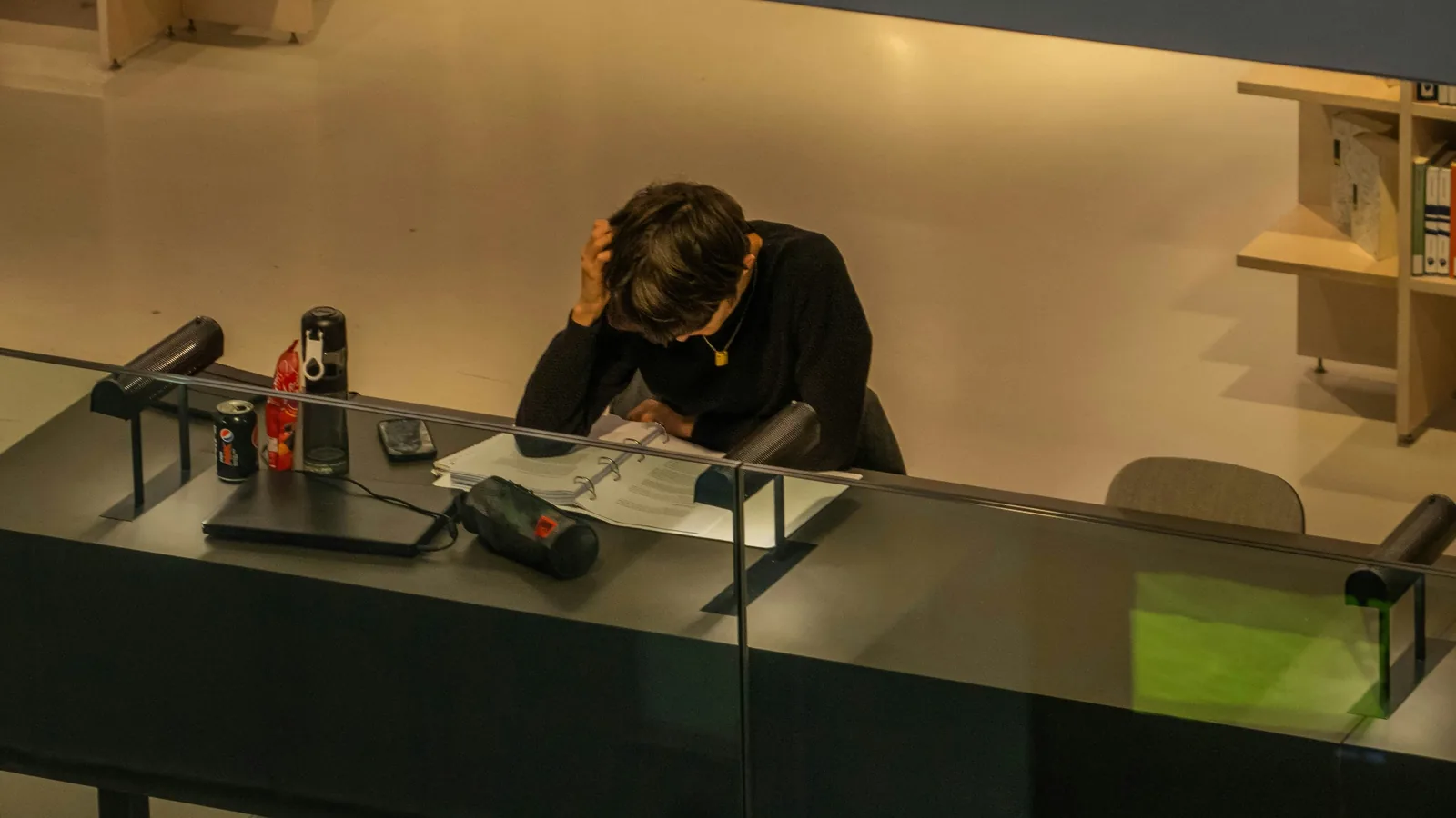 Une personne assise seule à un bureau, la tête dans les mains face à un classeur — la fatigue de la volonté isolée.
